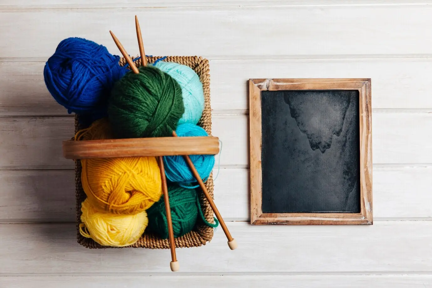 Verschiedene Wollknäuel in einem Korb neben einer Schieferplatte.